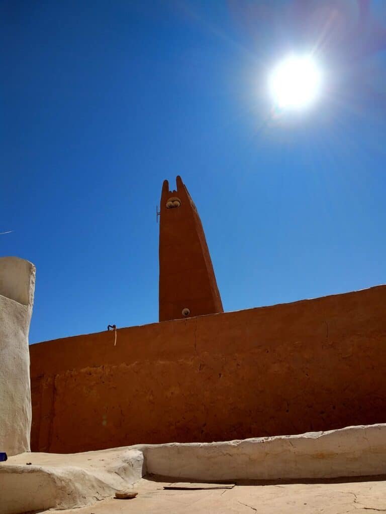 The Labyrinths of the M'zab Valley: In Search of the Cyclopes of Ghardaïa 6 The distinctive M'zab minaret of an Ibadi mosque rising against a deep blue Saharan sky in Ghardaïa — a tapering ochre earthen tower with finger-like corner merlons, emblem of Mozabite Berber architecture in Algeria's M'zab Valley pentapolis.